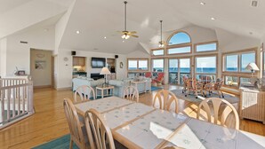 Un vaste espace de vie comprenant un coin repas avec une table et des chaises, ainsi qu’un balcon donnant sur la mer.