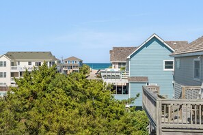 A coastal residential area with multiple two-story houses, a wooden deck, and a view of the ocean. - Shore'em Dreamin': Hot Tub, Community pool, Close to Beach, Pet-friendly (Nags Head)