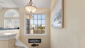 A hallway with a white ceiling, a large window with a view of a balcony, a fish decoration, and a 'happy place' sign. - A Change In Latitude: Pet-friendly! Shared Pool, Private Hot Tub (Nags Head)