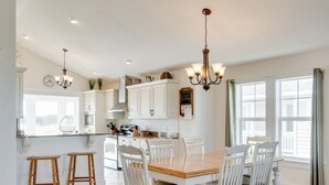 A spacious kitchen with white cabinetry, a wooden dining table, and bar stools. - Hook, Wine And Sinker: Private Pool, Hot Tub, Free Community Amenities! (Corolla)