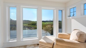 A room with a beige sofa and three large windows offering a view of a green landscape and a white fence. - Hook, Wine And Sinker: Private Pool, Hot Tub, Free Community Amenities! (Corolla)