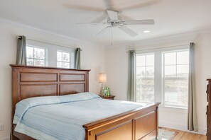 A bedroom with a wooden bed, a ceiling fan, and two windows with curtains. - Hook, Wine And Sinker: Private Pool, Hot Tub, Free Community Amenities! (Corolla)