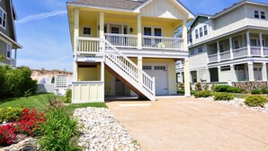 A two-story residential building with a front porch, a staircase leading to the second floor, and a garage. - Hook, Wine And Sinker: Private Pool, Hot Tub, Free Community Amenities! (Corolla)