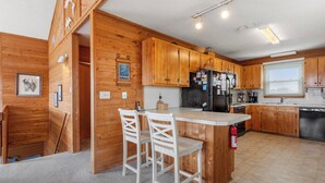 Una cocina con armarios de madera, un refrigerador, un lavamanos y dos taburetes de bar.