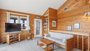 Una sala de estar acogedora con detalles de madera, un sofá, una mesa de centro, un televisor sobre un mueble bajo y una estantería.
