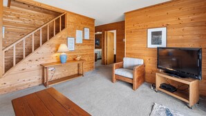 Un interior de madera con una escalera, un sofá, un televisor sobre un mueble bajo y una lámpara.