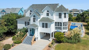 A large, multi-story house with a prominent front porch, a swimming pool, and a well-maintained garden. - Ebbtide: Private Pool, Screened Porch, Ocean Views (Corolla)