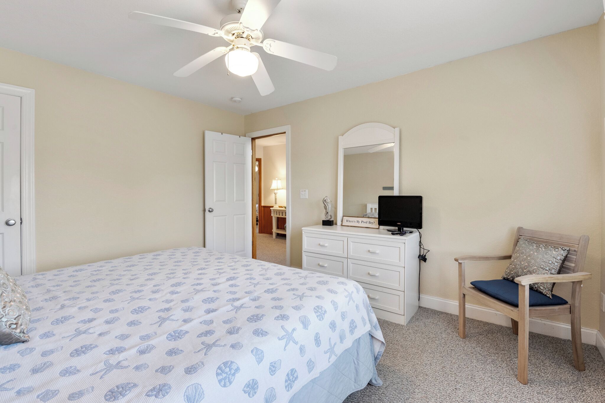 A bedroom with a bed, a dresser, a chair, a ceiling fan, and a mirror.