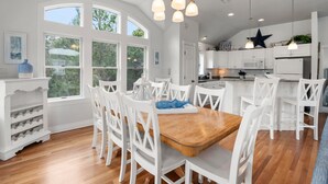 Une cuisine spacieuse avec des meubles blancs, une table à manger en bois et une grande fenêtre qui laisse entrer la lumière naturelle.