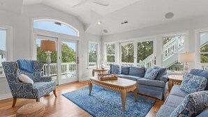 Un salon spacieux doté d’une grande fenêtre, d’un ventilateur de plafond et d’un tapis à motifs bleus.