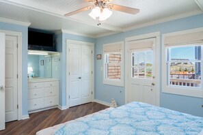 A bedroom with a bed, a ceiling fan, a window with a view, and a door.