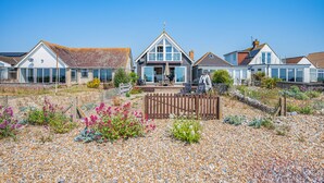 A row of coastal houses with a gravel driveway, a wooden fence, and various plants.
