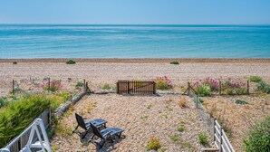 A pebbled beach with a wooden fence, a bench, and a small garden area.