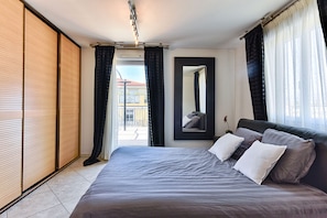 Une chambre à coucher moderne avec un grand lit, une porte coulissante, un miroir et une vue sur l’extérieur.