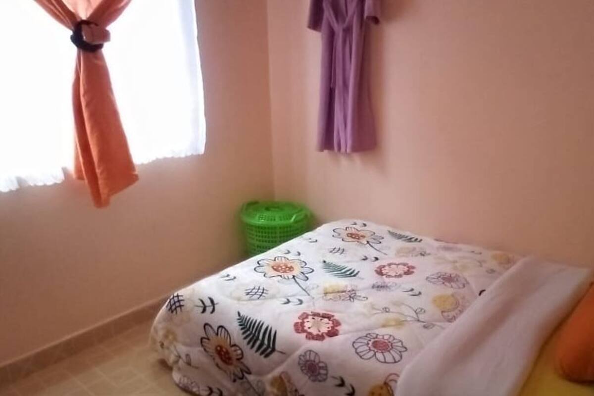 A bedroom with a bed, a window with curtains, a green trash bin, and a wall-mounted curtain.