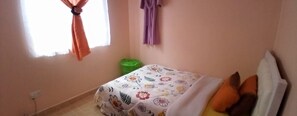 A bedroom with a bed, a window with curtains, a green trash bin, and a wall-mounted curtain.