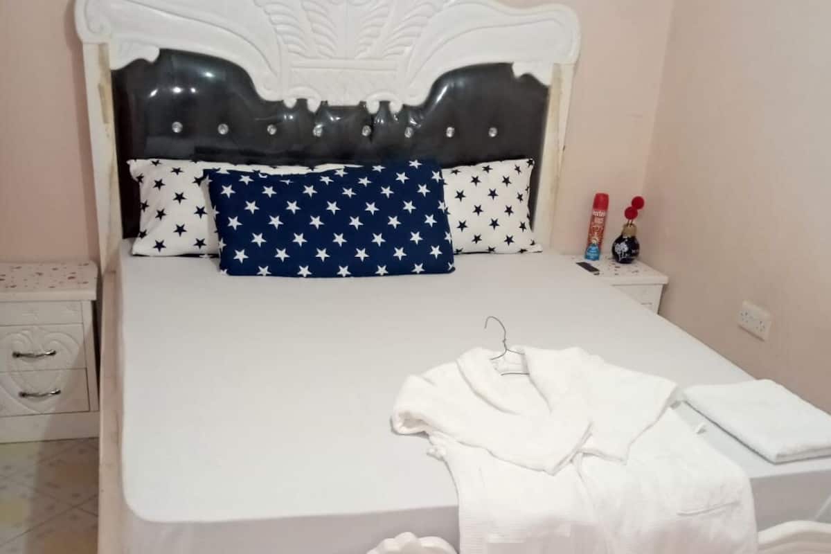 A neatly made bed with a white headboard and footboard, a blue pillow with white stars, and a white blanket.