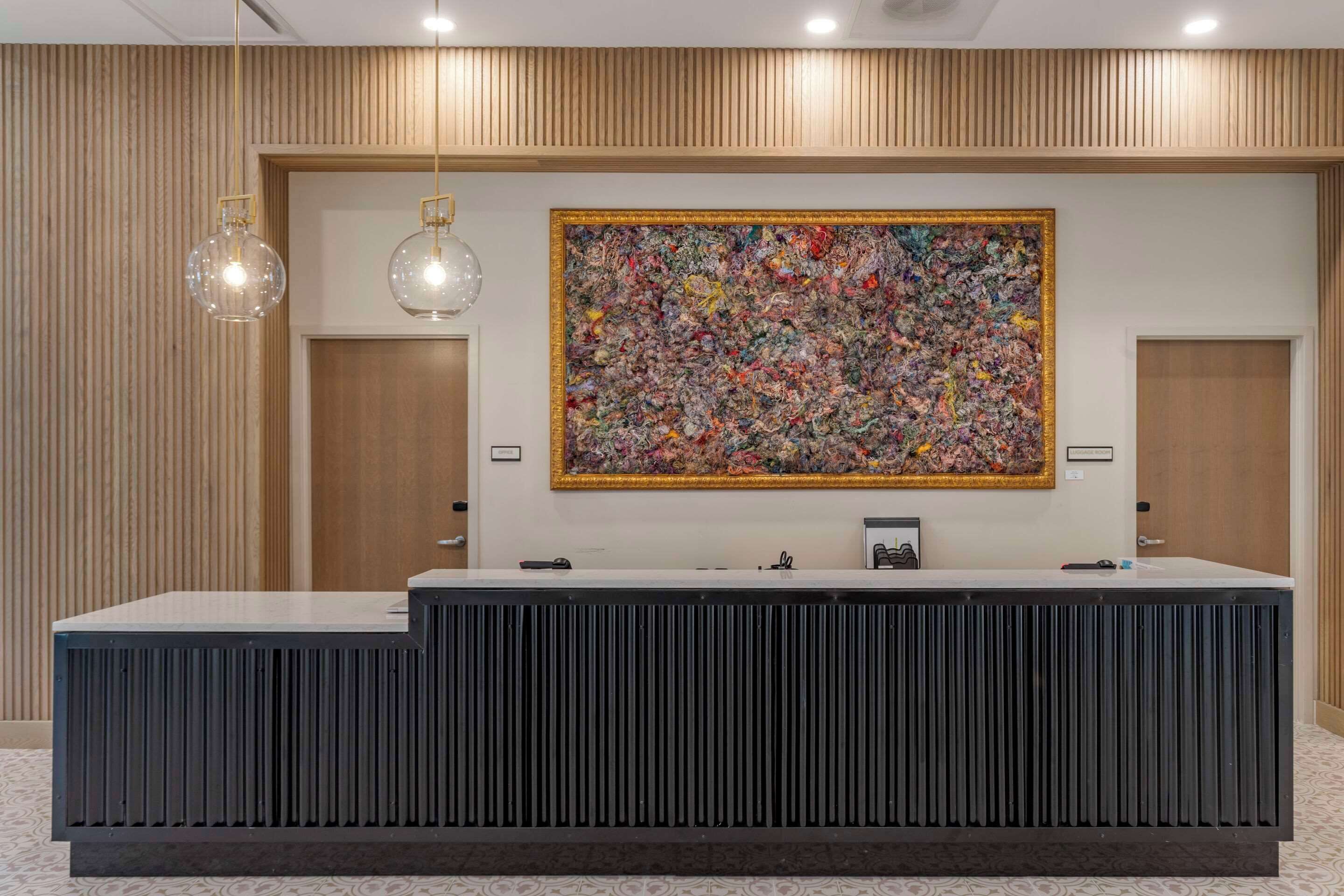 A reception desk with a large abstract painting above it, wooden paneling on the walls, and two doors.
