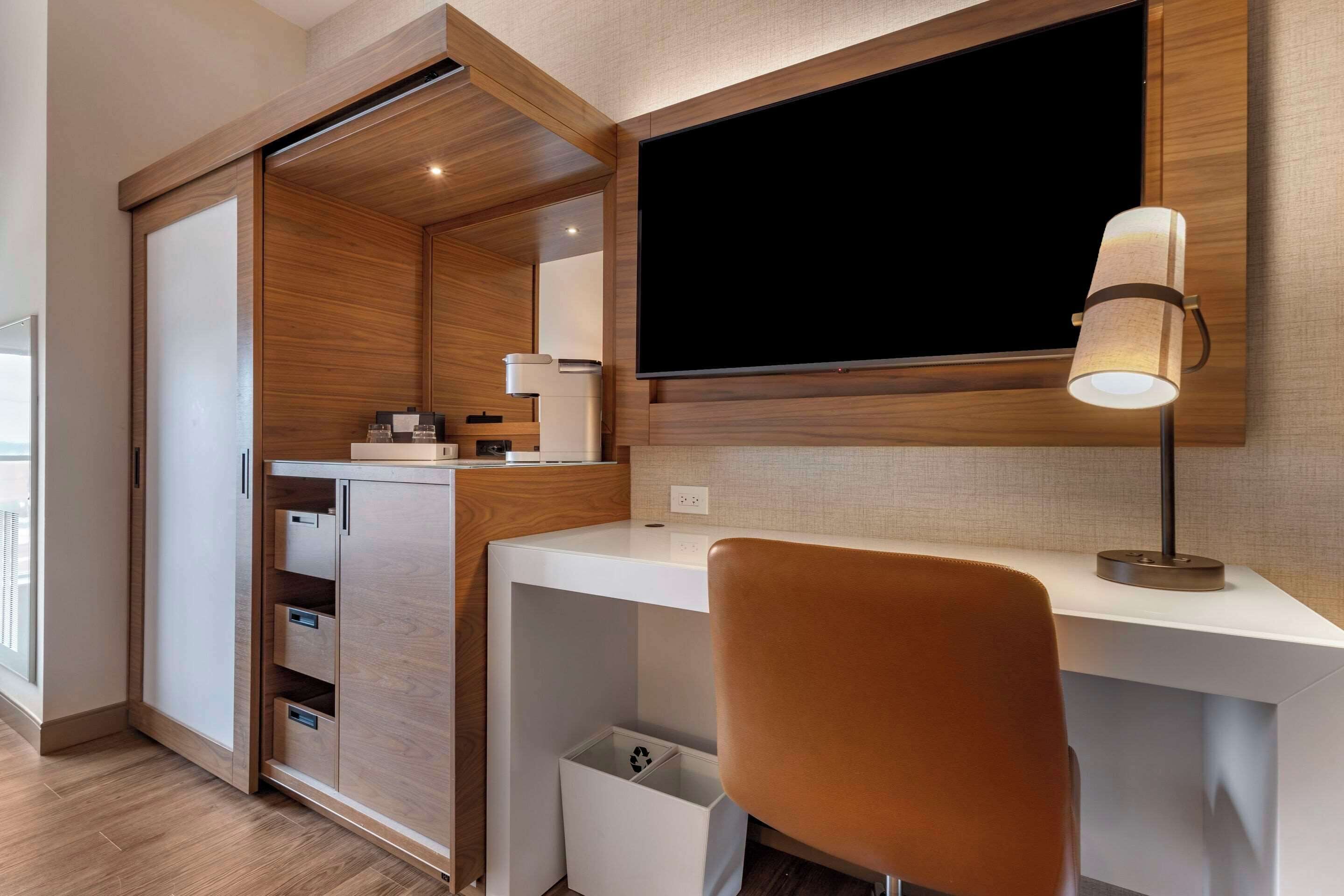 Ein modernes Zimmer mit Schreibtisch, Stuhl, Fernseher und integriertem Kleiderschrank.