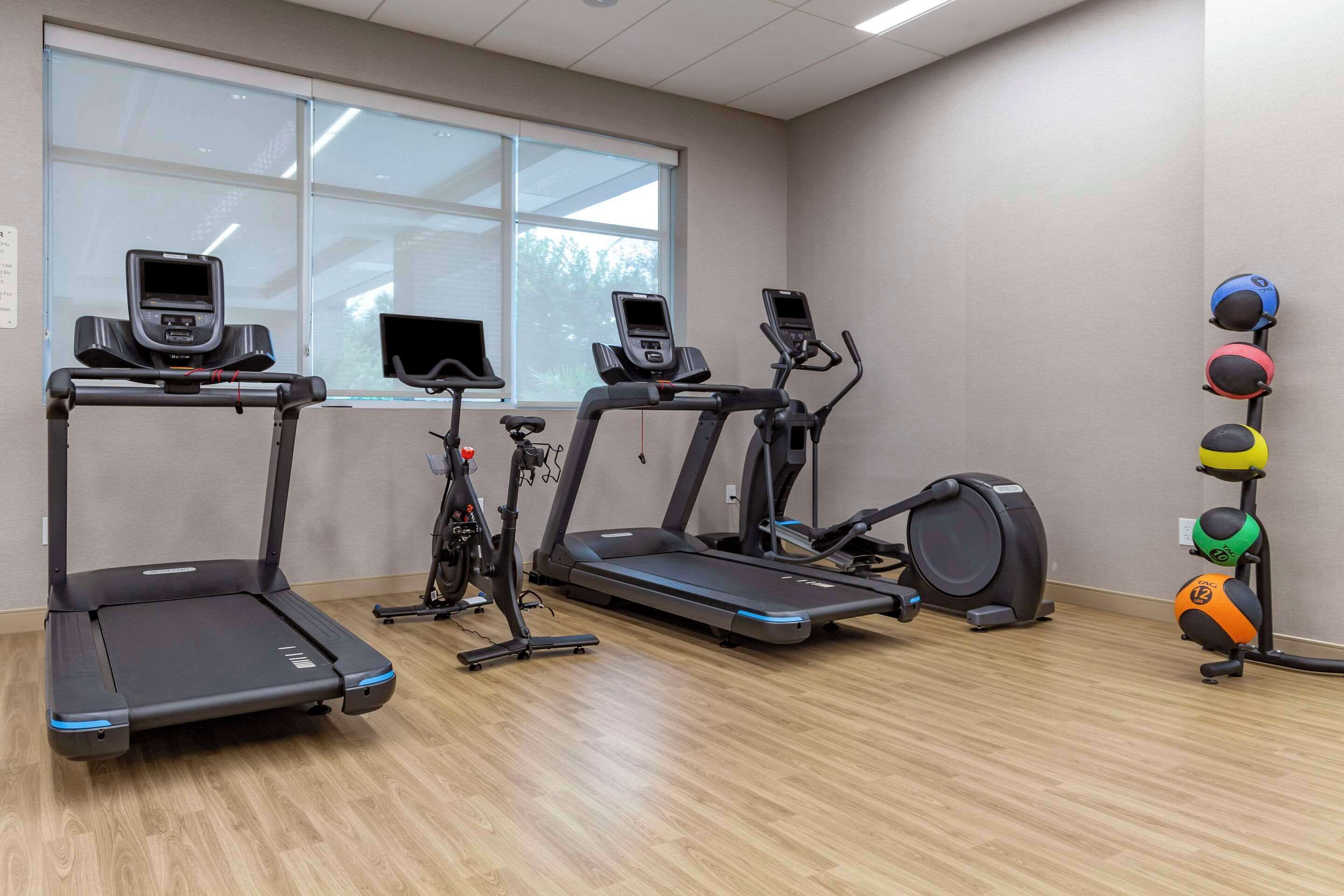 Un gimnasio con cintas de correr, una elíptica y un conjunto de pelotas de ejercicios.