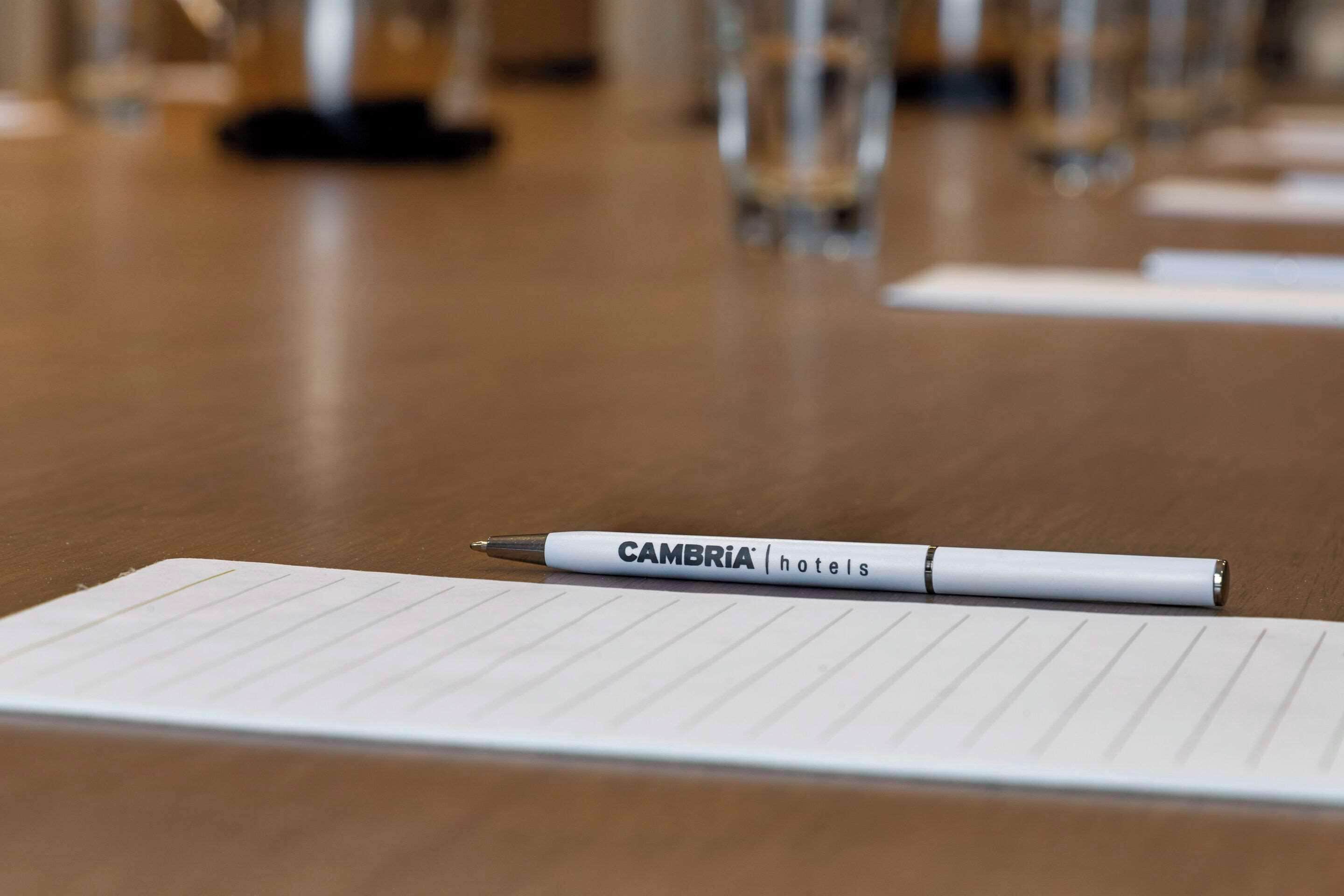 Una ploma blanca amb la inscripció 'CAMBRIA hotels' sobre un quadern amb línies damunt d'un taulell de fusta.