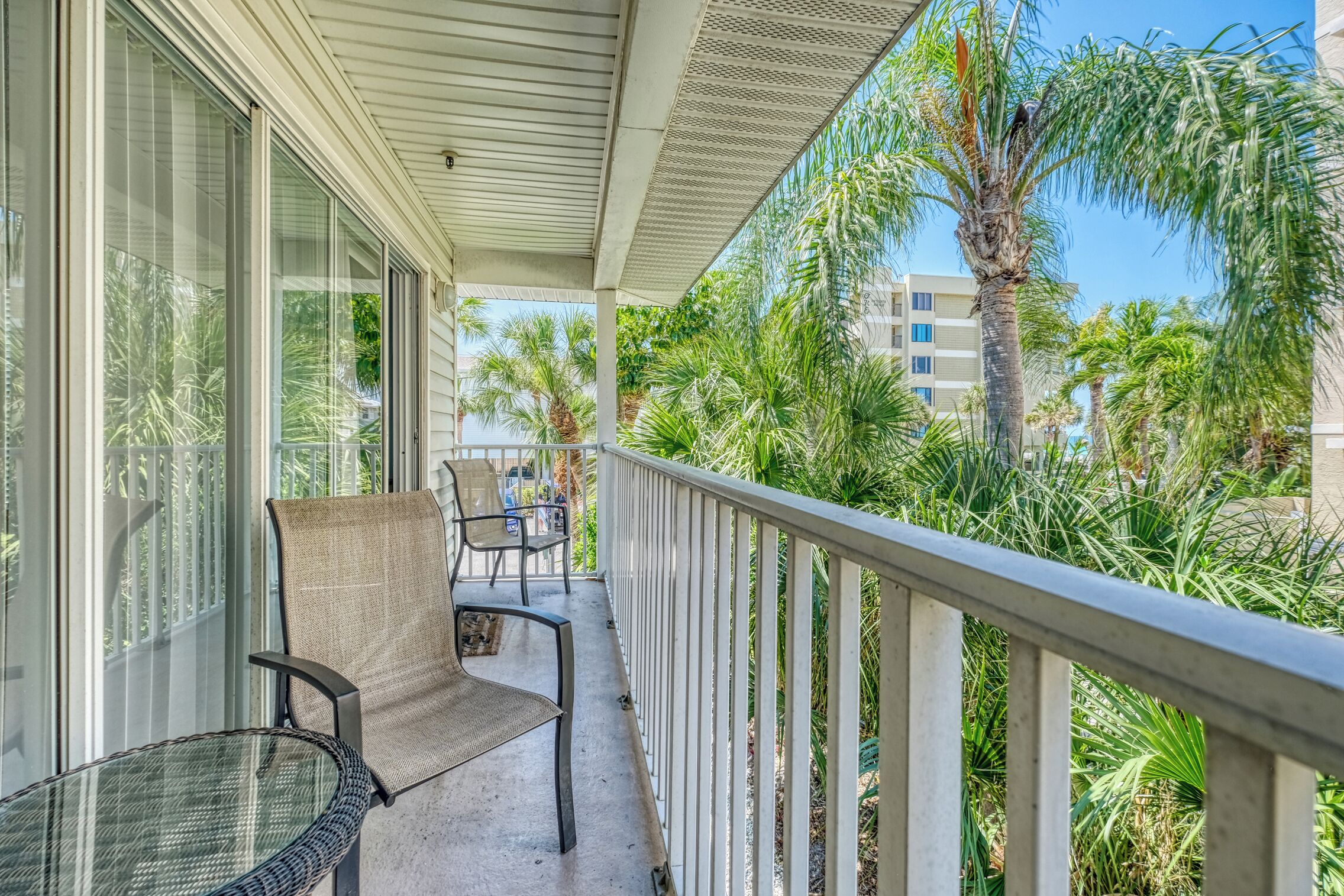 A balcony with a chair and table, overlooking a palm tree and building.