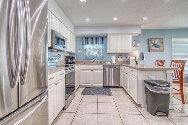 A modern kitchen with stainless steel appliances, white cabinetry, and a tiled floor.