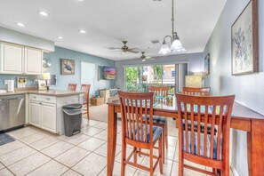 A kitchen with a dining area, wooden chairs, ceiling fans, and a view of the outdoors. - You and Me and the Sea: 2  BR, 2  BA Condominium in Indian Rocks Beach, Sleeps 4 (Indian Rocks Beach)