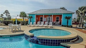 A swimming pool with a hot tub, surrounded by lounge chairs and a small building with a red and blue facade. - Great Cottage~Perfect Destination for an amazing Vacation!!! (Gulf Shores)