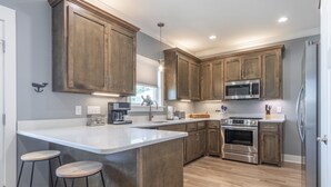 A modern kitchen with wooden cabinets, stainless steel appliances, and a central island with stools. - Great Cottage~Perfect Destination for an amazing Vacation!!! (Gulf Shores)