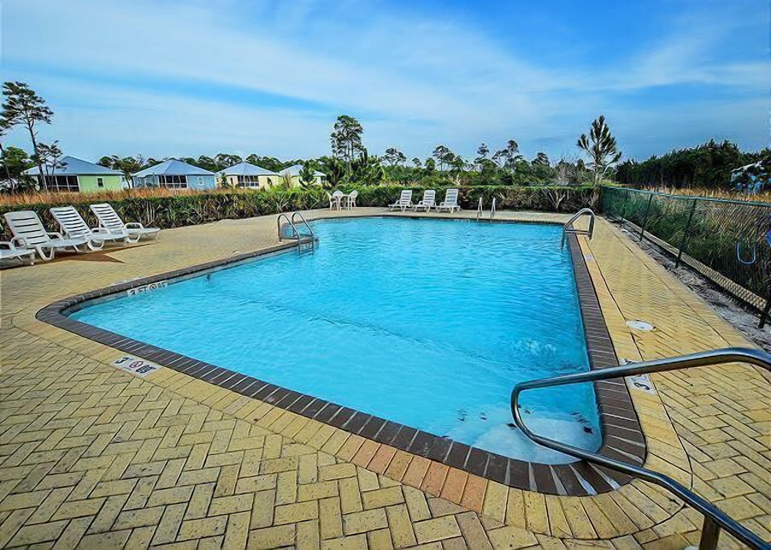 A rectangular swimming pool with a tiled deck, surrounded by lounge chairs and a fence.