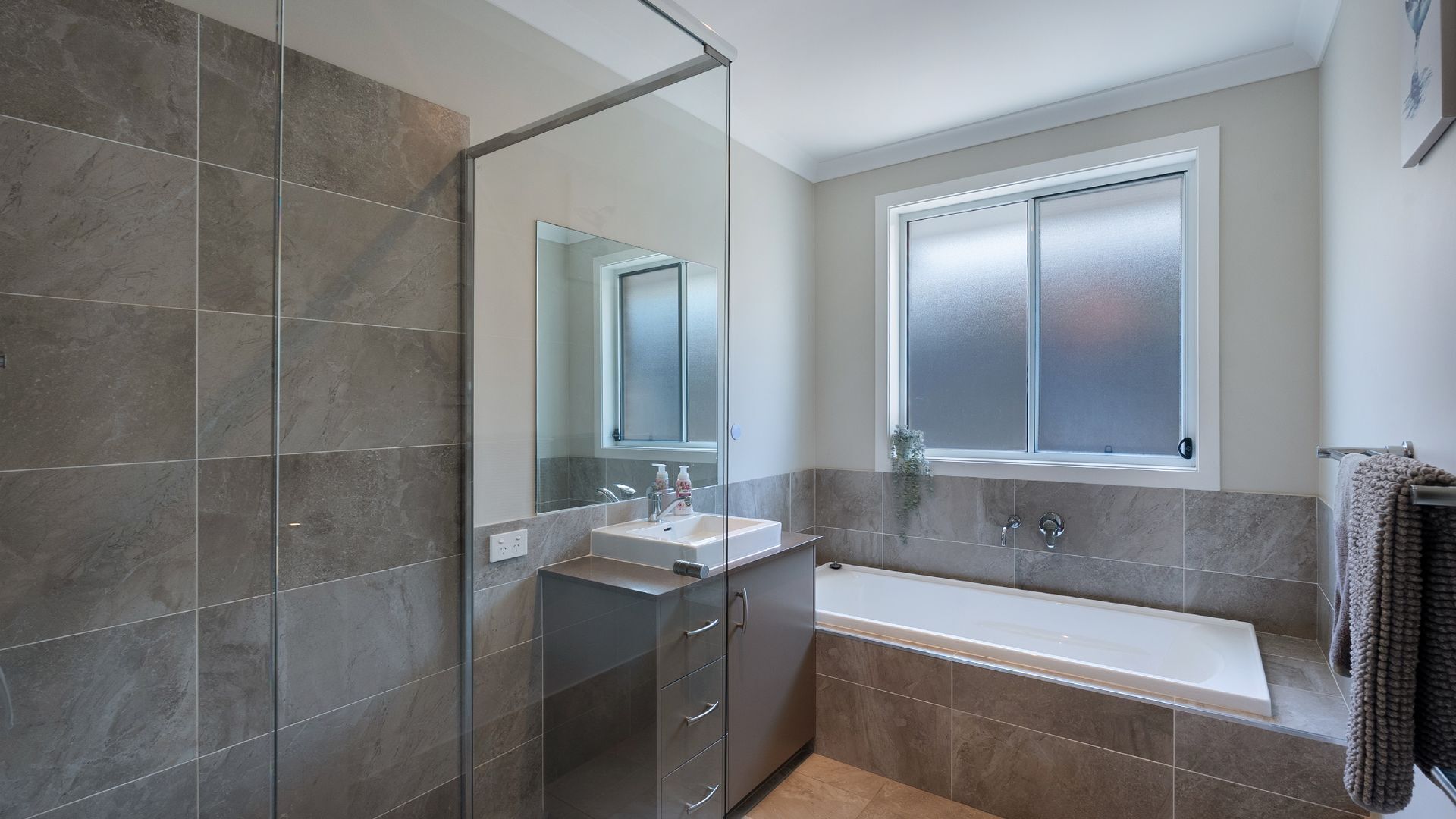 A modern bathroom with a glass shower enclosure, a freestanding bathtub, and a vanity with a mirror.