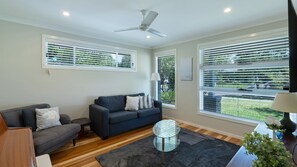 A modern living room with a grey sofa, a round glass coffee table, and a ceiling fan. - Charis by the Bay by Book Jervis Bay (Vincentia)