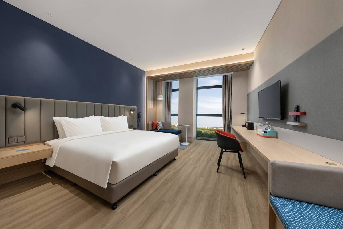 A modern hotel room with a large bed, a desk, a chair, and a TV.