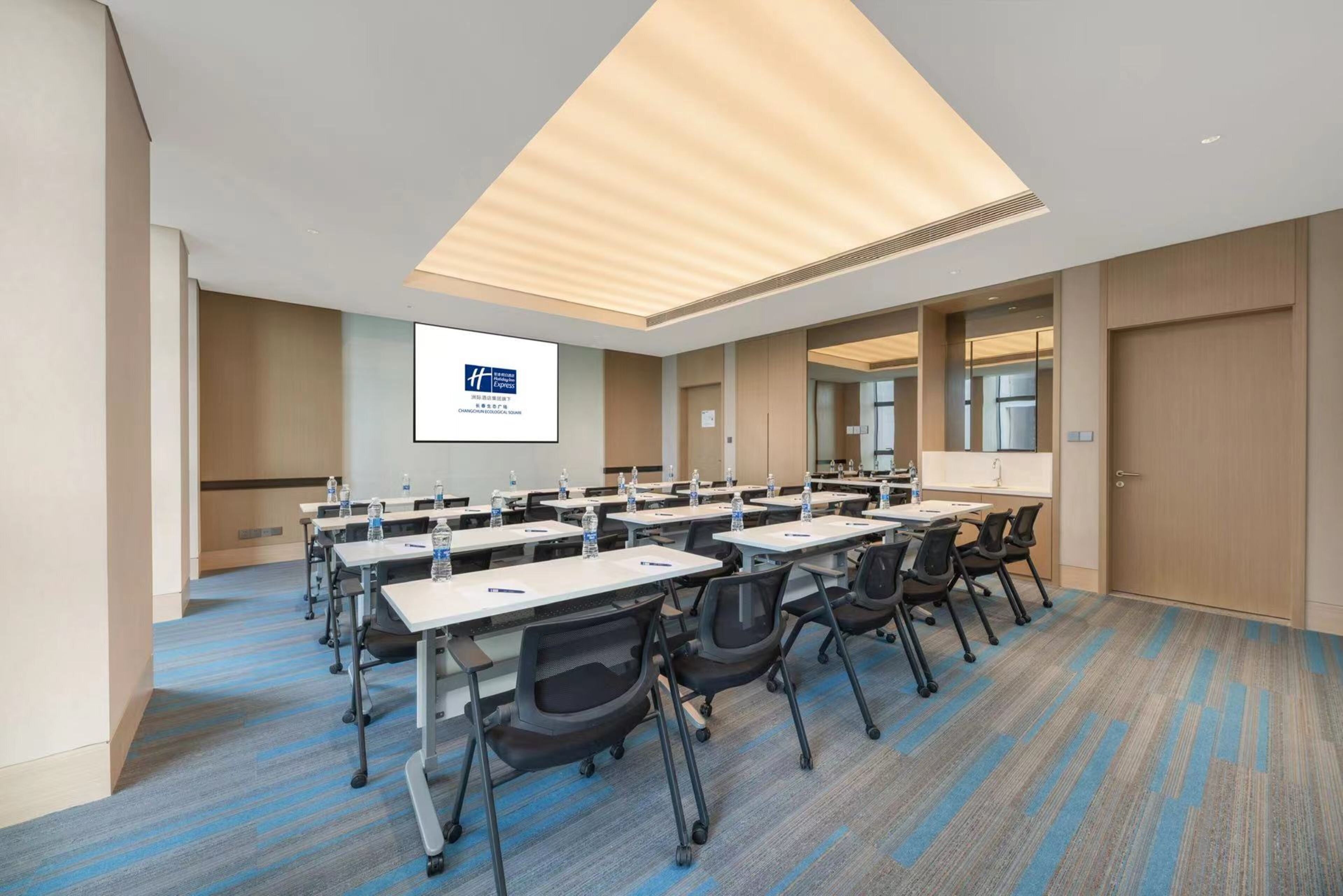 A conference room with multiple tables, chairs, and a projection screen.
