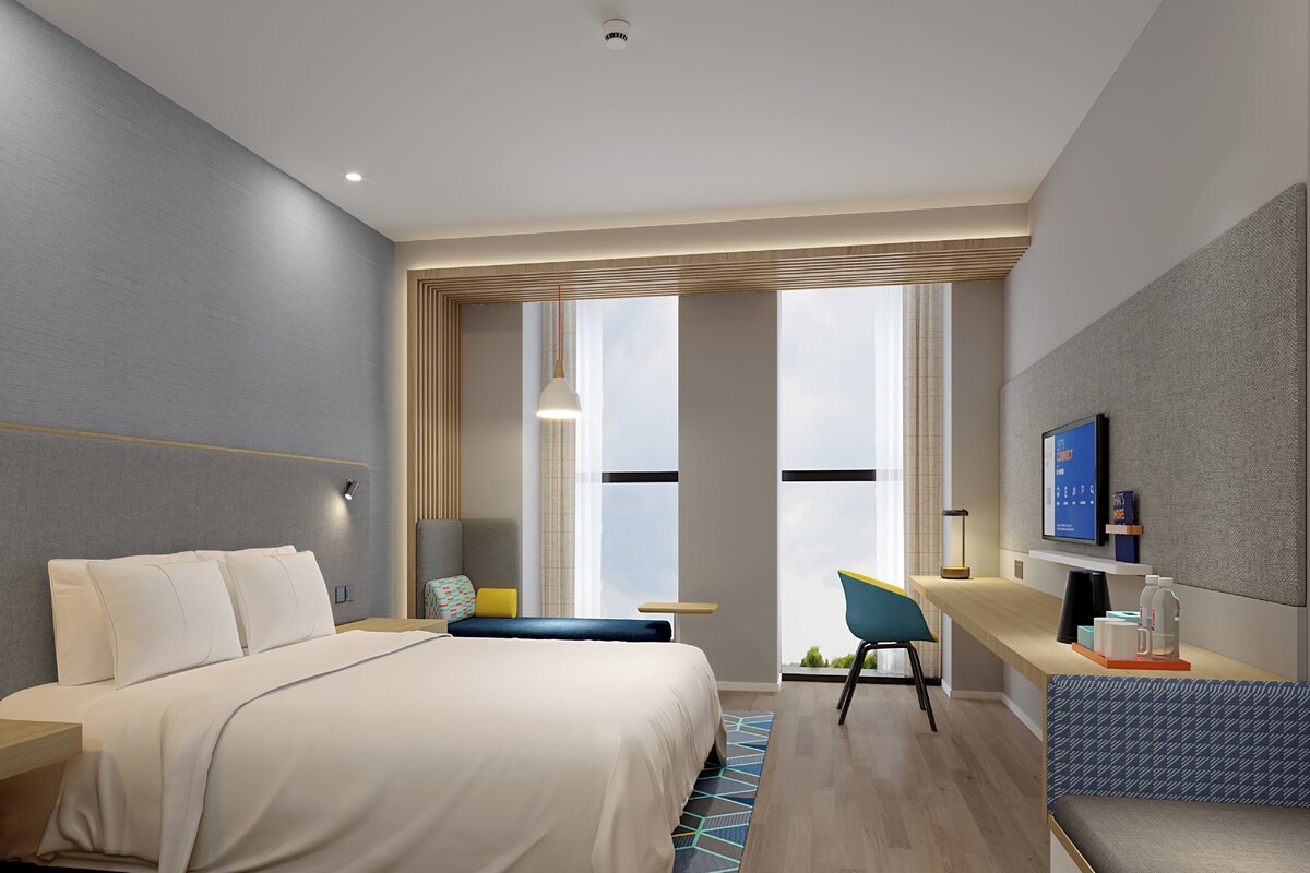 Ein modernes Hotelzimmer mit Bett, Schreibtisch, Stuhl und Fernseher.