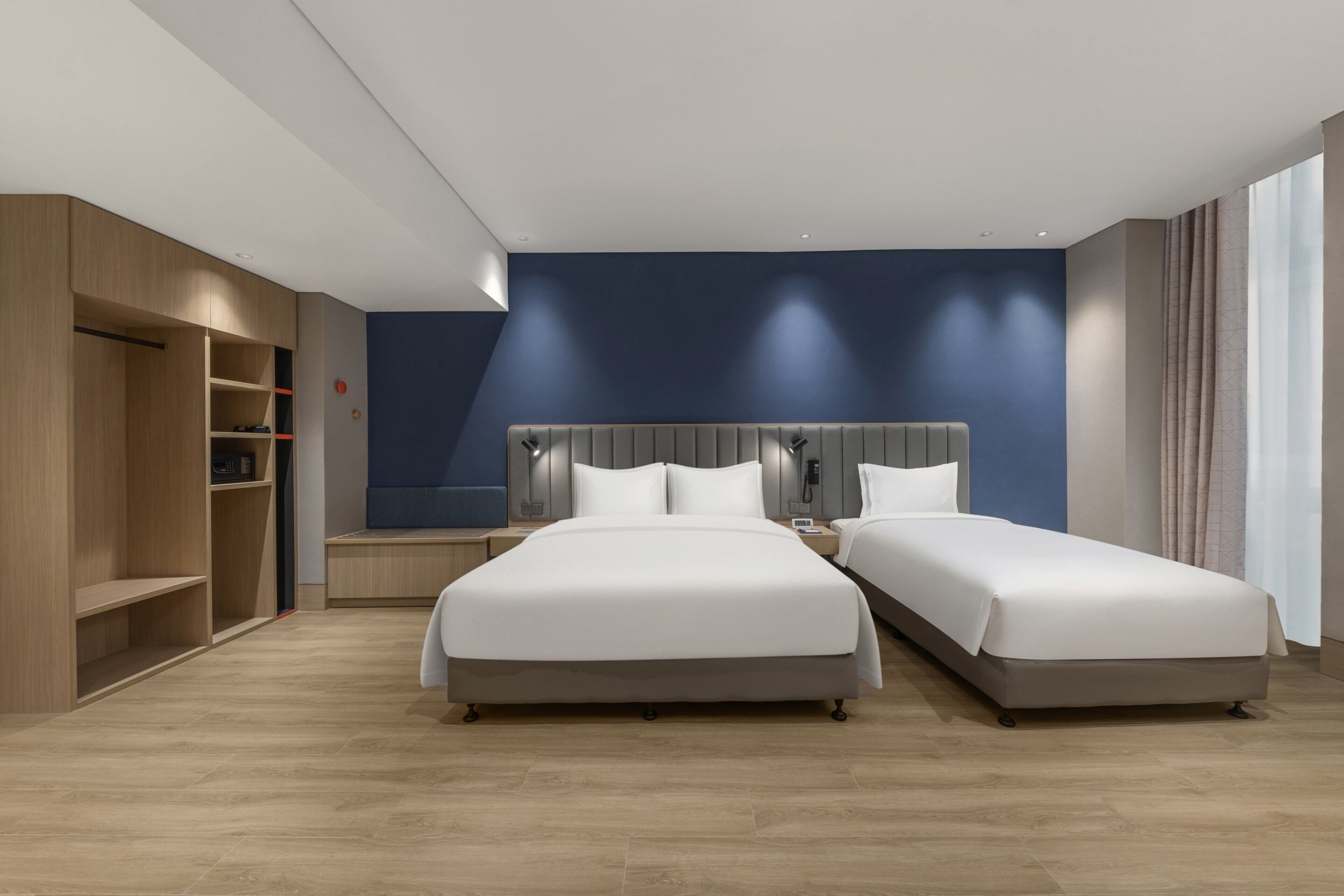 A modern hotel room with two beds, a wardrobe, and a desk.