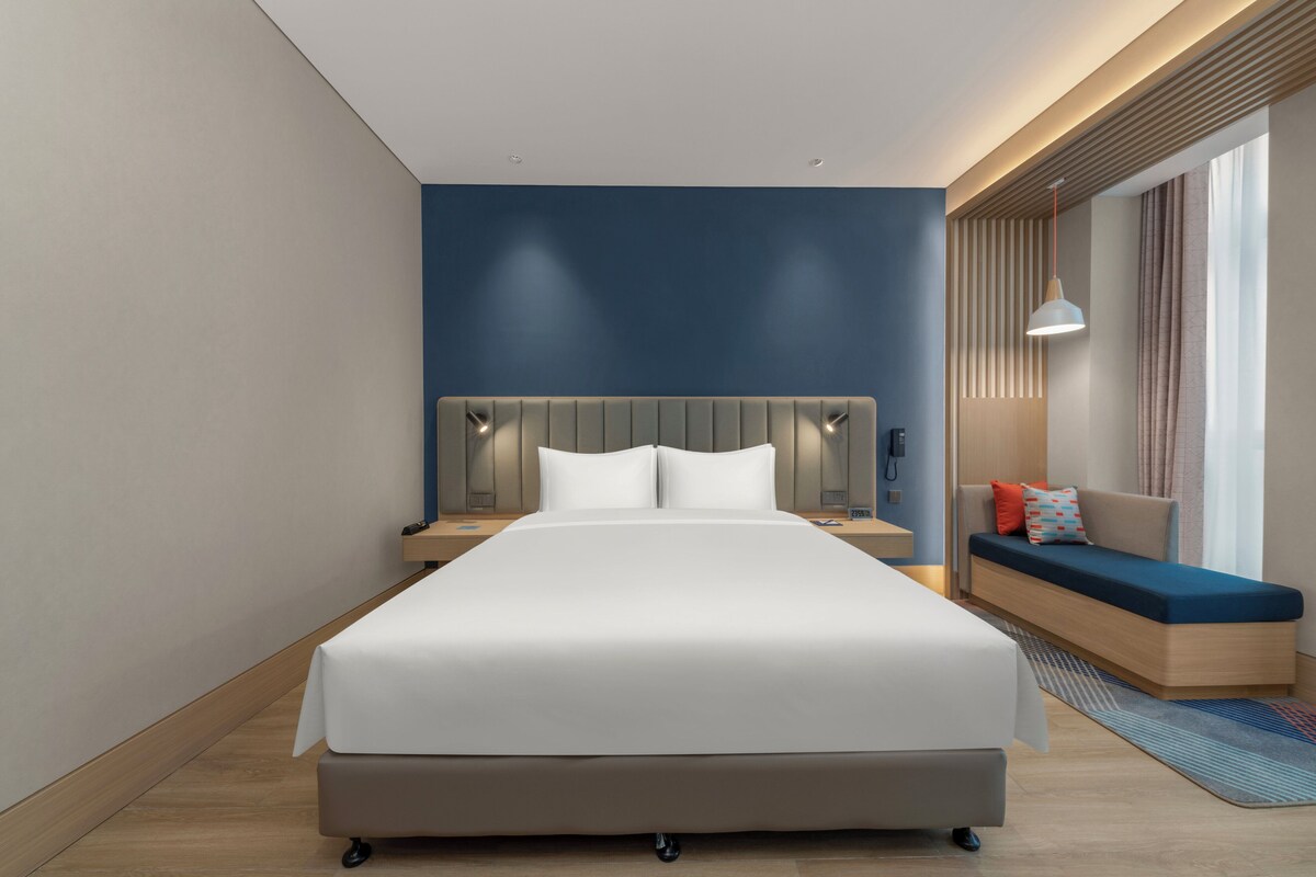 Ein modernes Hotelzimmer mit einem großen Bett, Nachttischen, einer eingebauten Bank und Blick ins Freie.