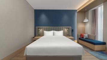 Una habitación de hotel moderna con una cama grande, mesitas de noche, un banco incorporado y vistas al exterior.