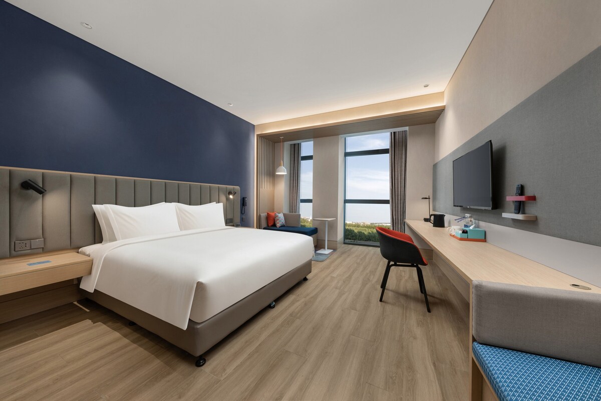 Ein modernes Hotelzimmer mit Bett, Schreibtisch, Stuhl und einem großen Fenster mit Blick.