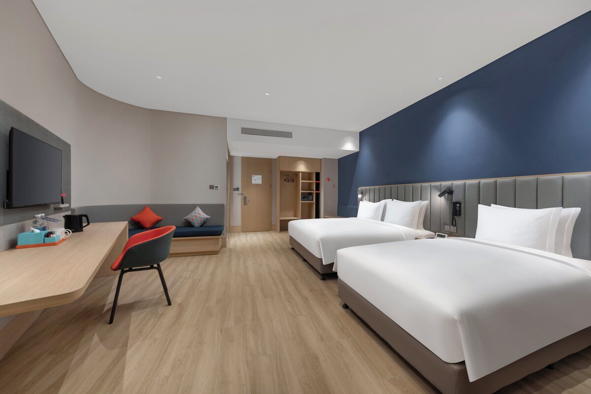 Ein Hotelzimmer mit zwei Betten, einem Schreibtisch, einem Stuhl, einem Fernseher und einem Kleiderschrank.