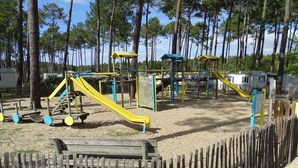 Ein Spielplatz mit Rutschen und Klettergerüsten, umgeben von einem Holzzaun und Bäumen.