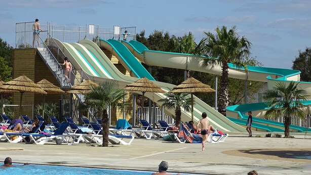 Ein Wasserpark mit mehreren Rutschen, Liegestühlen und einem Schwimmbecken.
