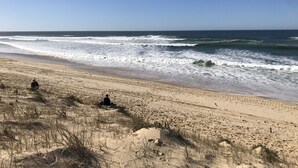 Ein Strand mit blauem Himmel, Wellen und Fußabdrücken im Sand.