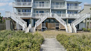 A multi-story beachfront property with a wooden deck leading to a set of stairs.