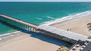A beachside pier with a covered seating area and tables, overlooking the ocean.