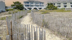 A beachfront property with a sandy path leading to a multi-story building with balconies.