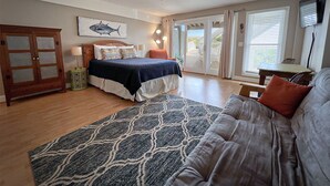 A bedroom with a bed, a ceiling fan, a large window, and a view of the outdoors.