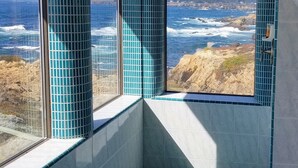 A bathroom with a view of the ocean. It features a window with blue-tiled walls and a shower area.