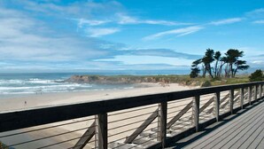 A wooden boardwalk leading to a beach with a view of the ocean and cliffs.